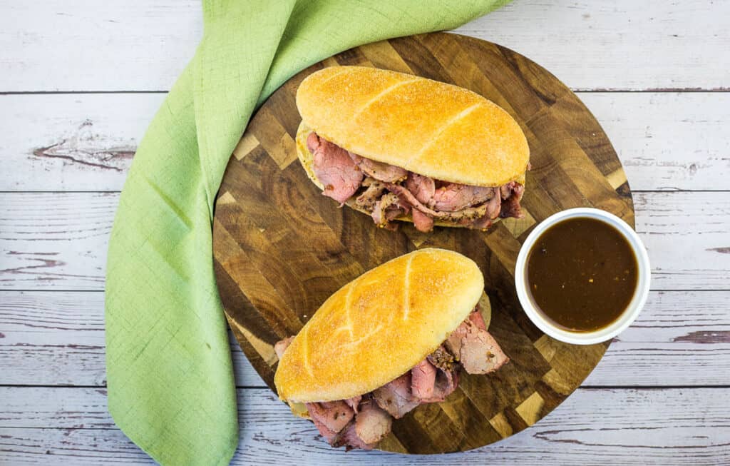 A horizontal top-down shot of 2 Smoked French Dip Sandwiches on a board.