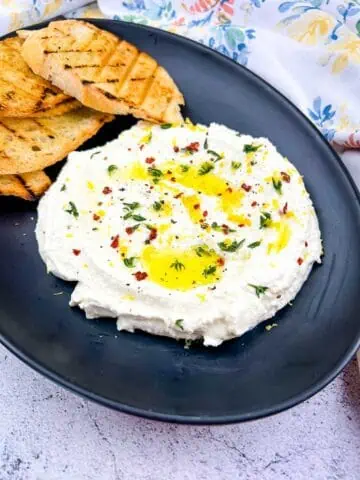 Whipped feta on a black plate with toasted bread in the background.