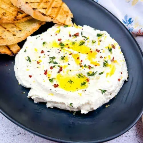 Whipped feta on a black plate with toasted bread in the background.