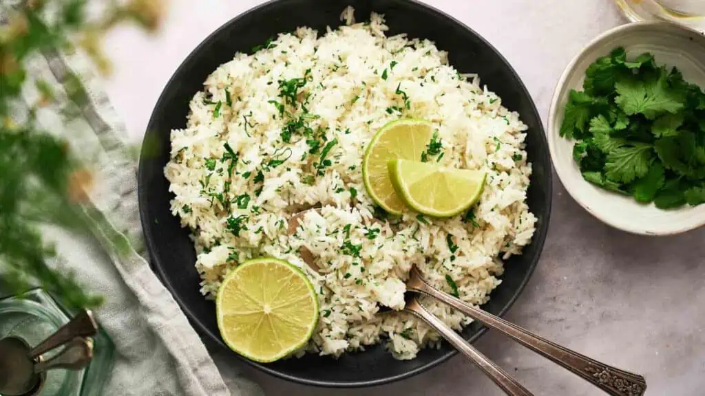 A bowl of rice with lime slices on it and serving spoons.