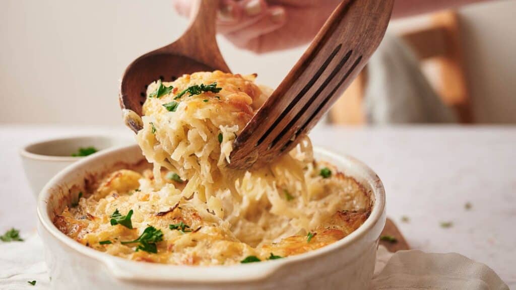 Someone dishing up hashbrown casserole.