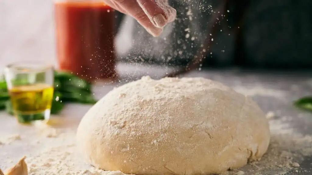 Someone sprinkling flour over a pizza dough ball.