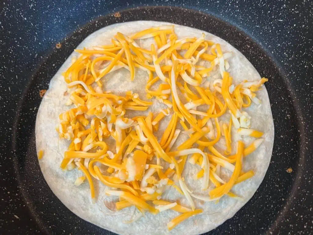 First tortilla in a skillet topped with cheese.