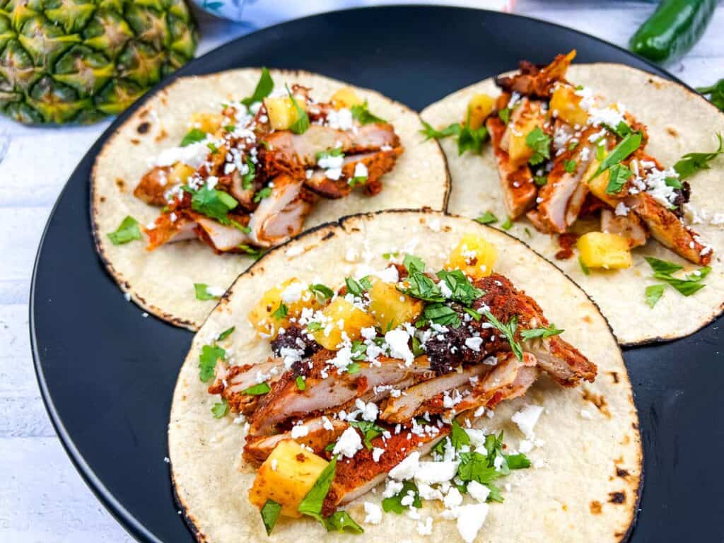 Smoked Chicken Al Pastor Tacos on a black plate.