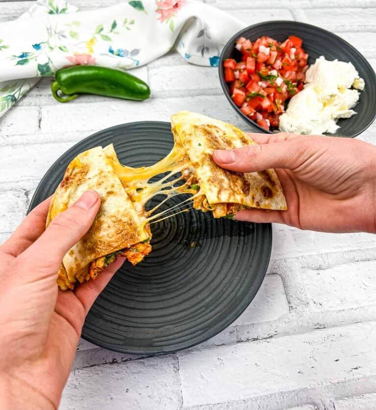 Two hands pulling apart a Chicken Al Pastor Quesadilla.