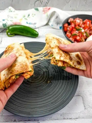 A horizontal shot of two hands pulling the quesadilla apart with gooey cheese in the middle.