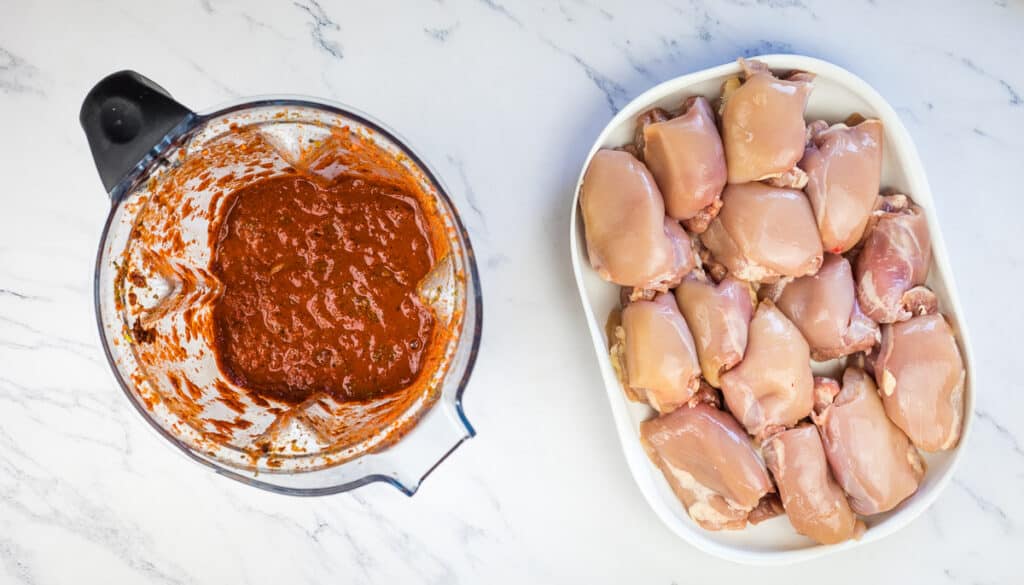 Chicken marinade in a blender next to chicken thighs.