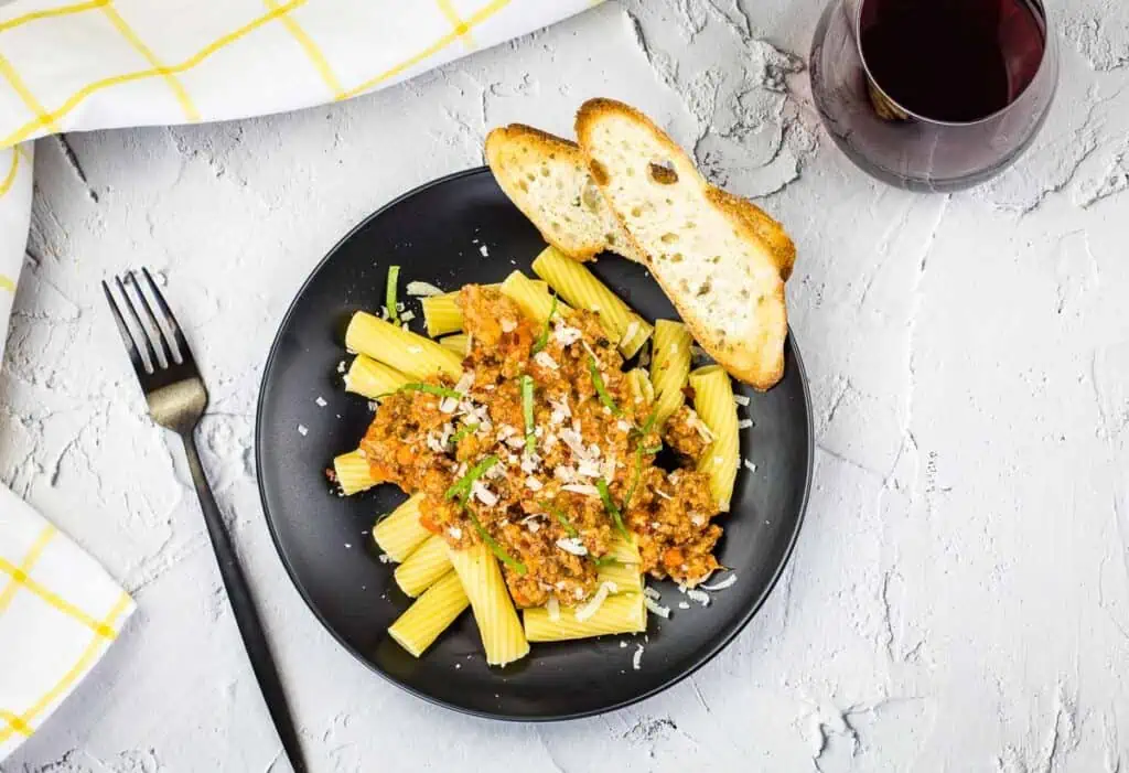 Authentic Bolognese Sauce on pasta on a black plate with bread.