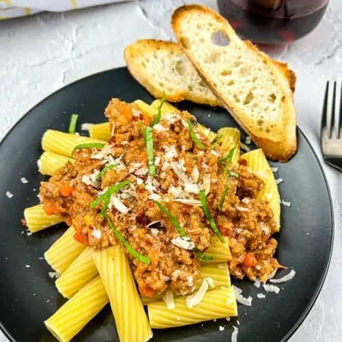 Authentic Bolognese Sauce on pasta on a black plate with bread.
