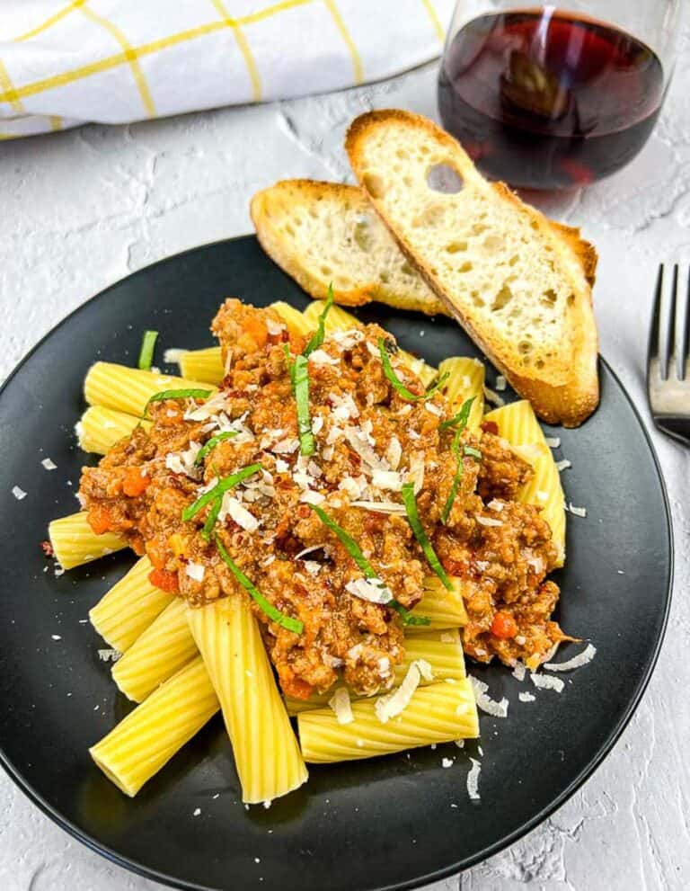 Authentic Bolognese Sauce on pasta on a black plate with bread.