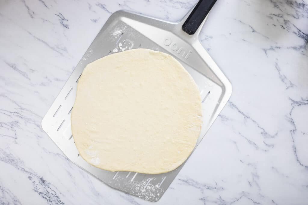 Rolled pizza dough on a pizza paddle.