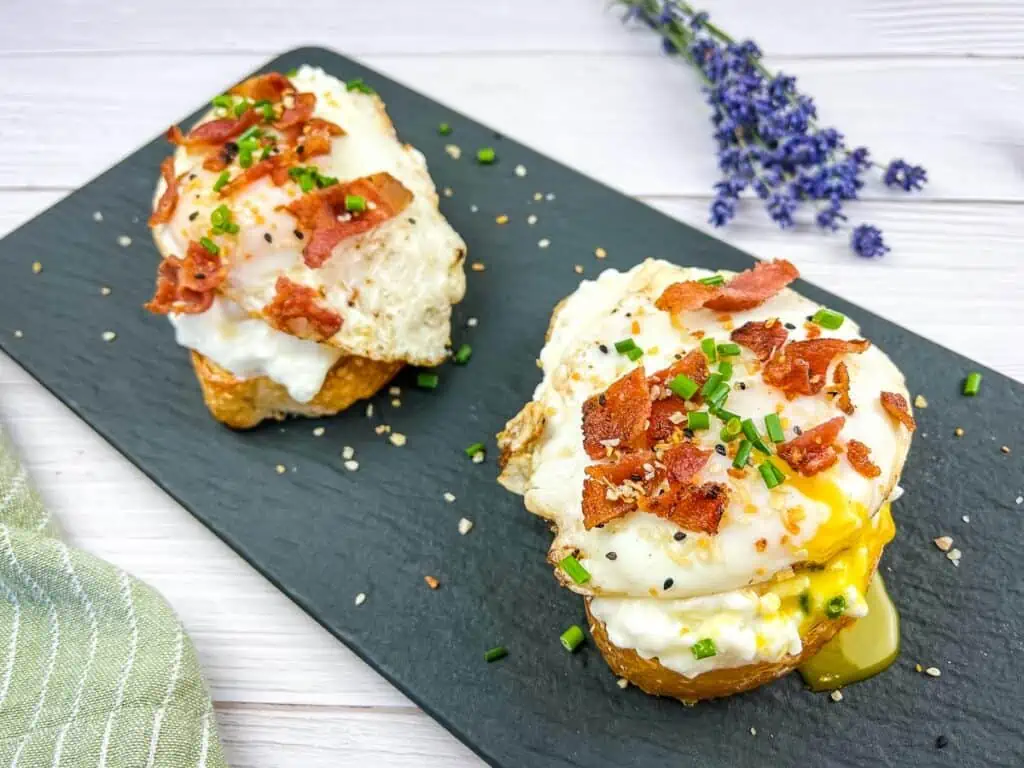 Two servings of Cottage Cheese Toast with Sunny-Side Up Egg and Bacon on a black platter.