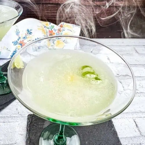 Smoked Gimlet in a glass with smoke coming off the top of it.