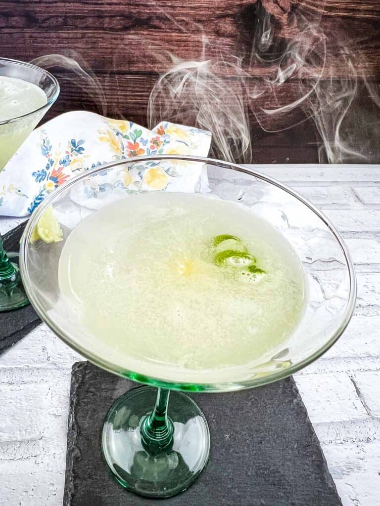 Smoked Gimlet in a glass with smoke coming off the top of it.
