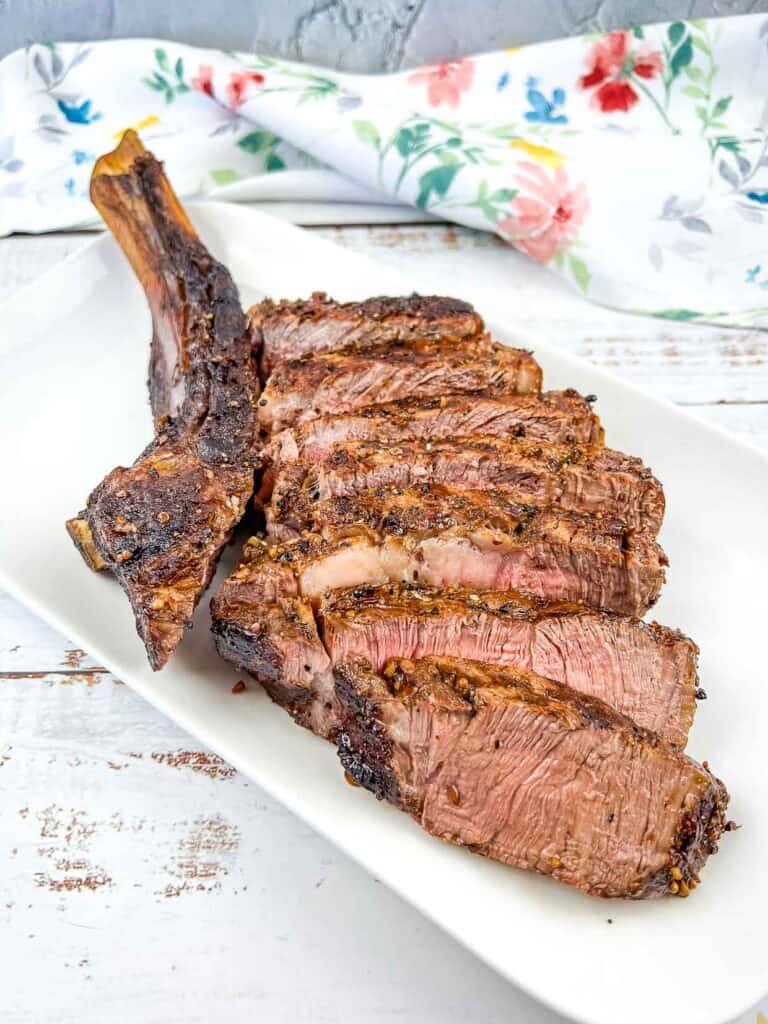 A tomhawk steak cooked on the Ninja Woodfire Grill. Sliced and served on a white platter.