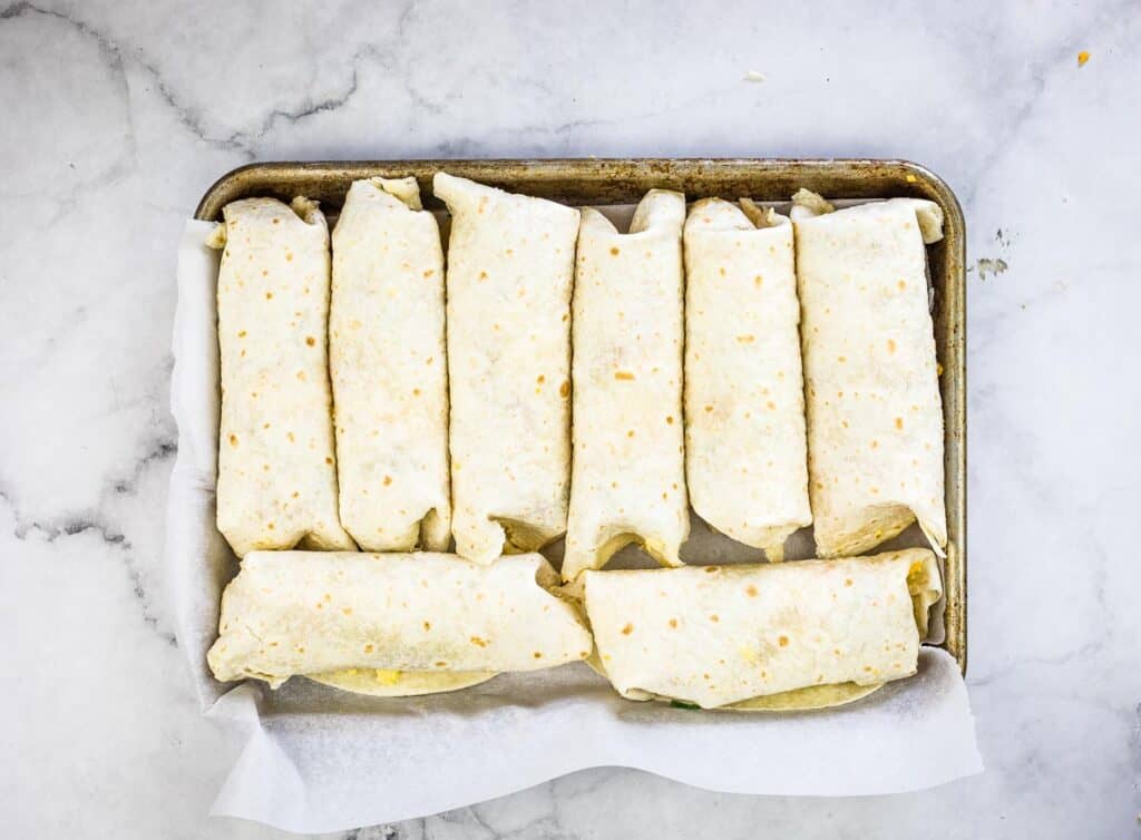 Rolled burritos on a baking sheet ready for freezing.