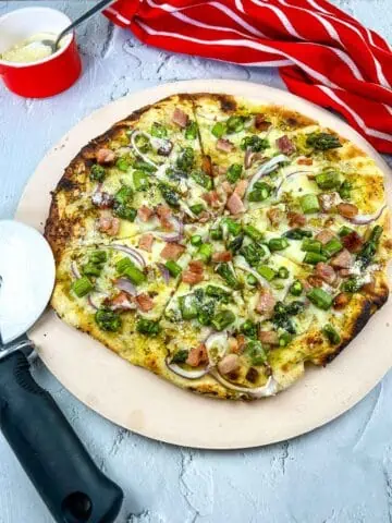 Vertical image of a Ham and Asparagus pizza on a pizza stone.