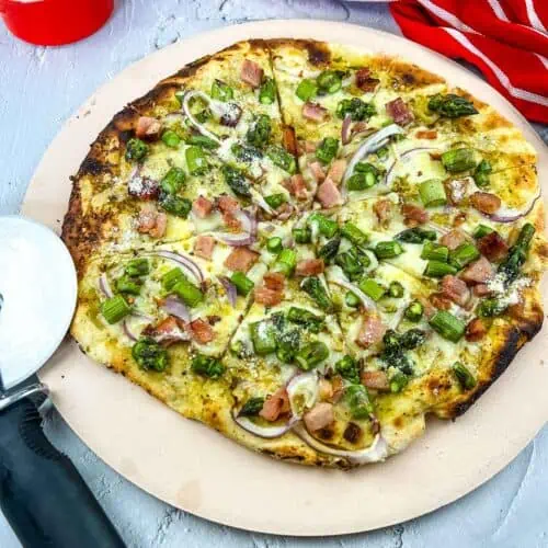Vertical image of a Ham and Asparagus pizza on a pizza stone.