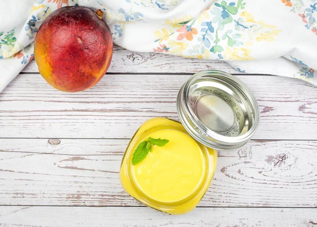 Mango curd in a jar with a mango nearby.