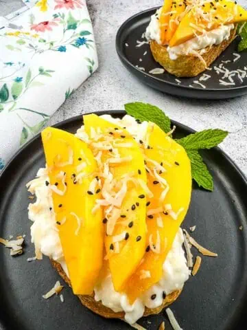 Cottage Cheese Toast with Mango and Coconut on a black plate with a second in the background.