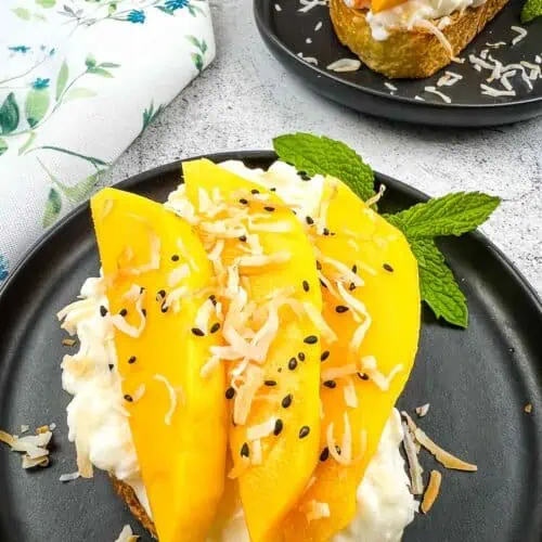 Cottage Cheese Toast with Mango and Coconut on a black plate with a second in the background.