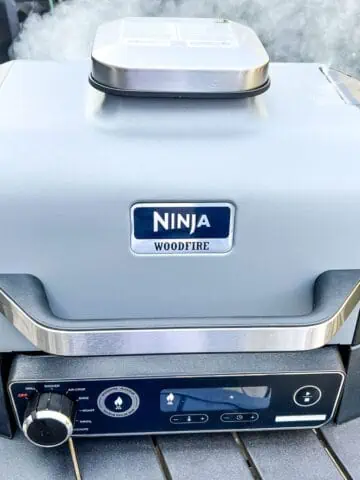 An image of a closed Ninja Woodfire Grill with smoke coming out of it.