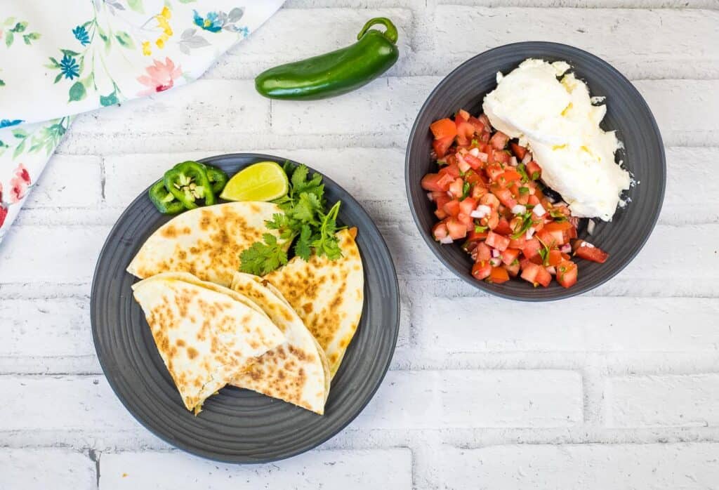 A top-down shot of Chicken Al Pastor Quesadillas cut in wedges with salsa nearby.