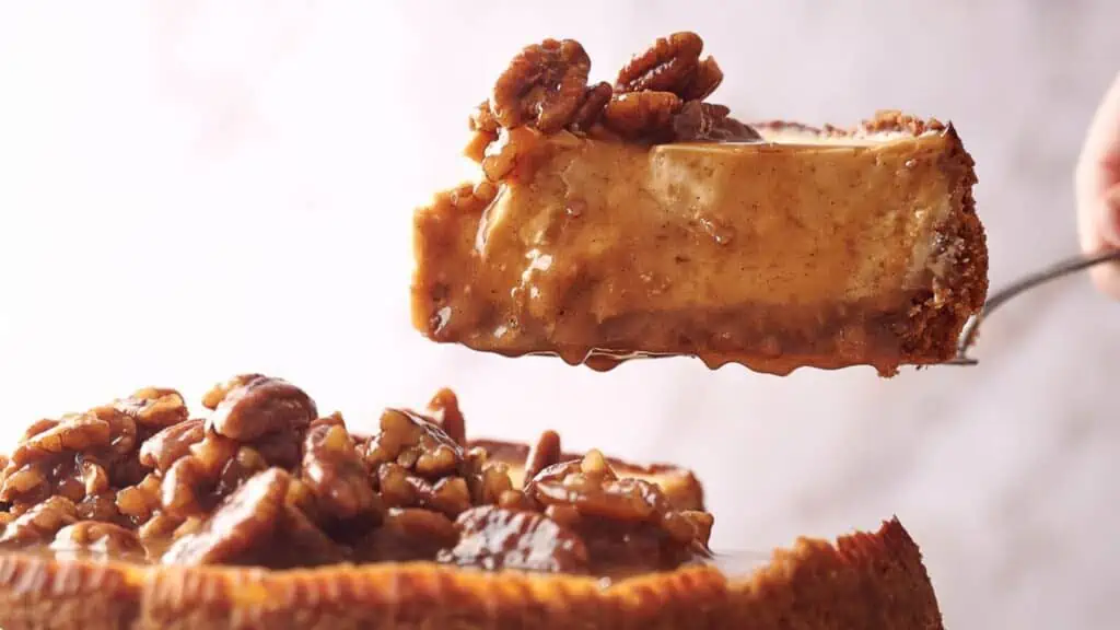 Someone serving a slice of pecan cheesecake.