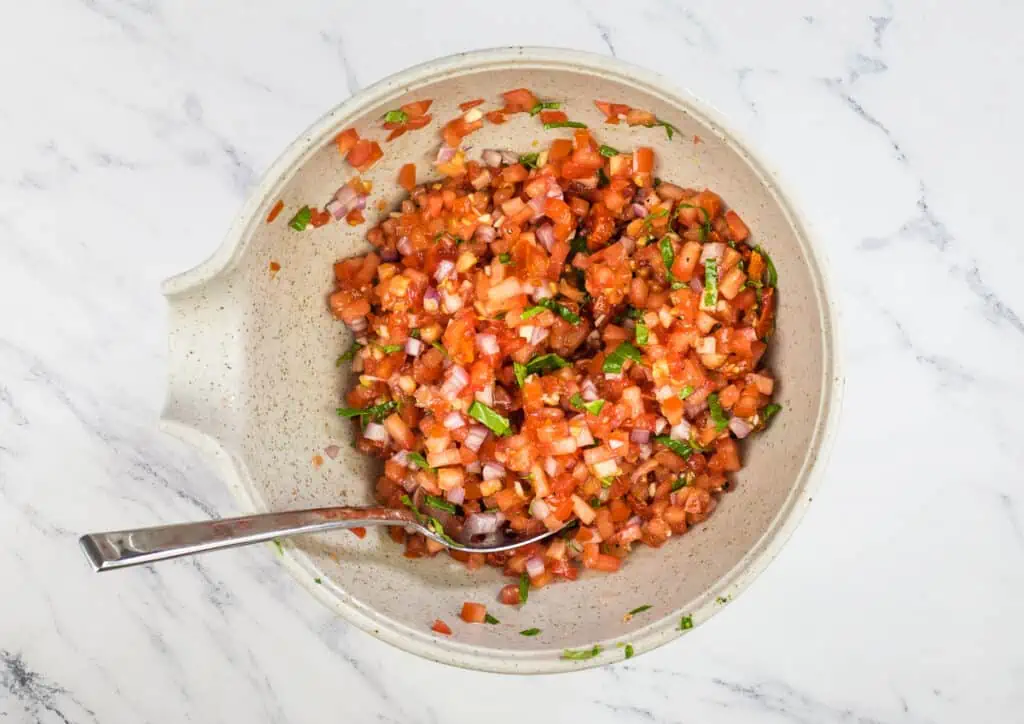 Mixed tomato bruschetta mixture in a bowl with a spoon.