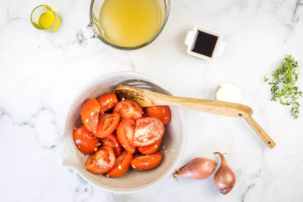 Tomatoes tossed with salt and pepper and garlic in a bowl.