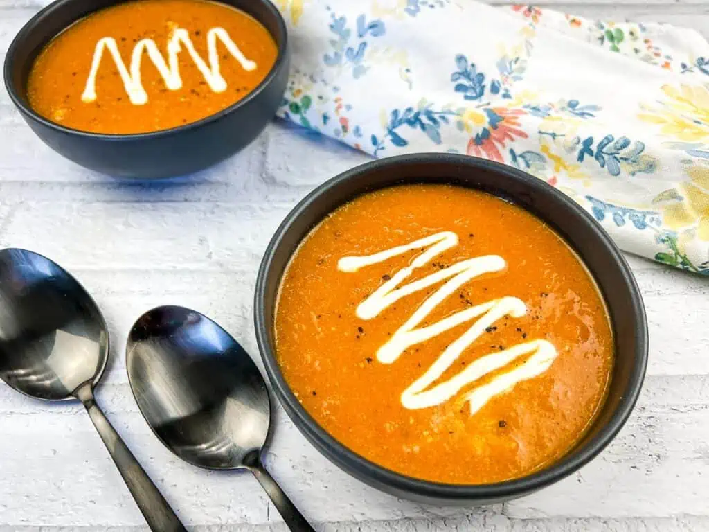 Two bowls of smoked tomato soup with spoons.