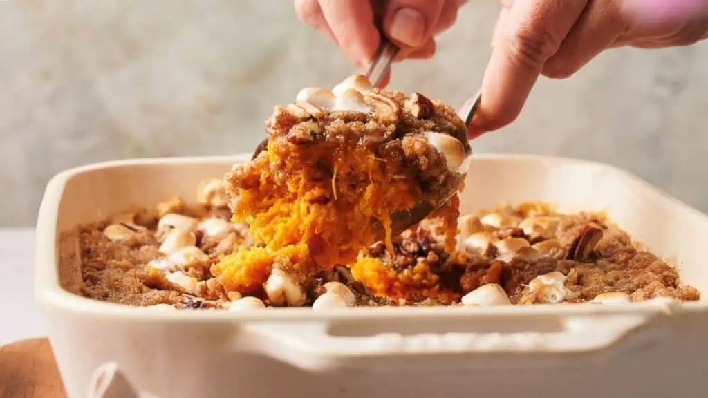 Someone dishing a serving of sweet potato casserole from a baking dish.