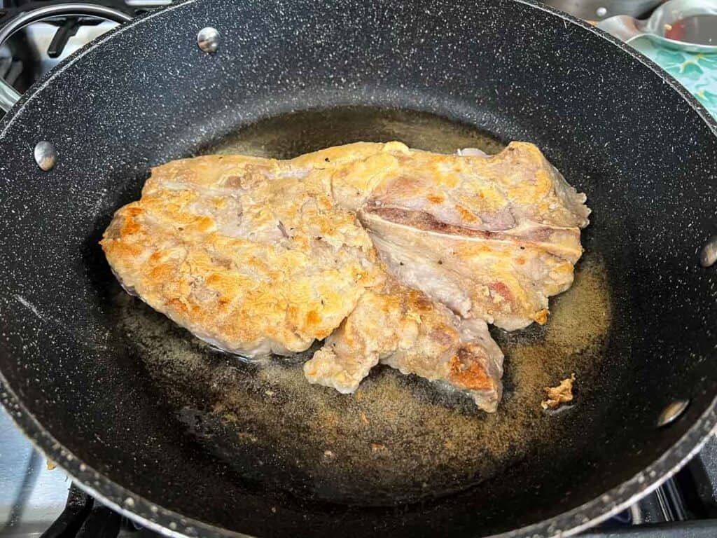 A dredged pork chop browning in a skillet.