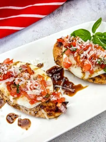 Two chicken breasts on a white plate with tomatoes and basil.