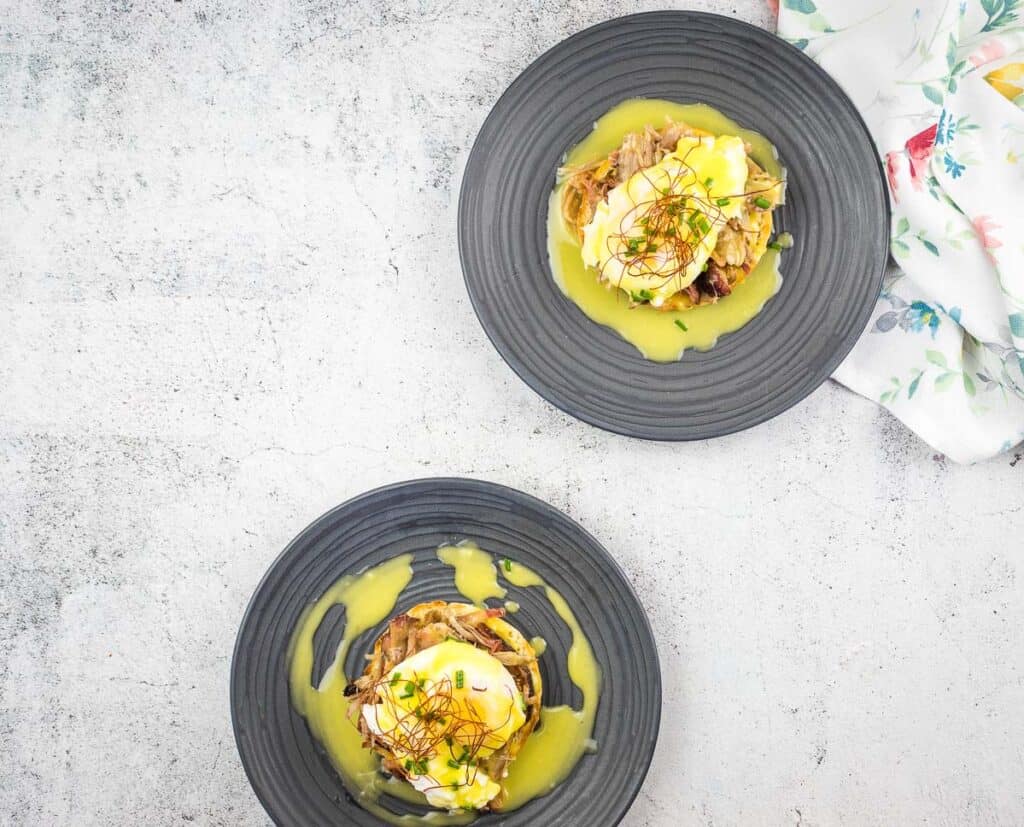 Two plates of pulled pork eggs benedict with a sauce on them.
