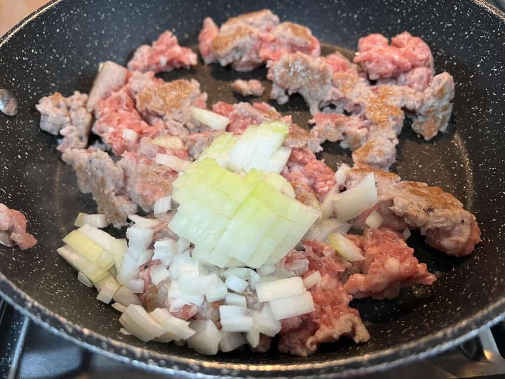 A frying pan with onions and meat in it.