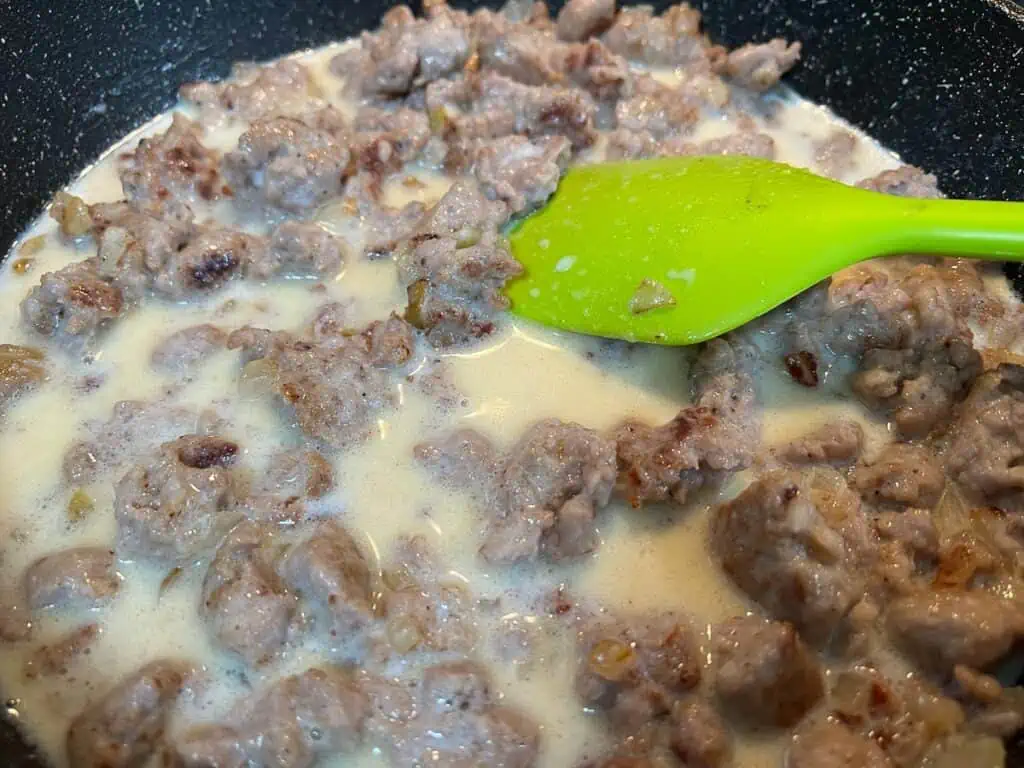 Sausage gravy in a skillet with a green spatula.