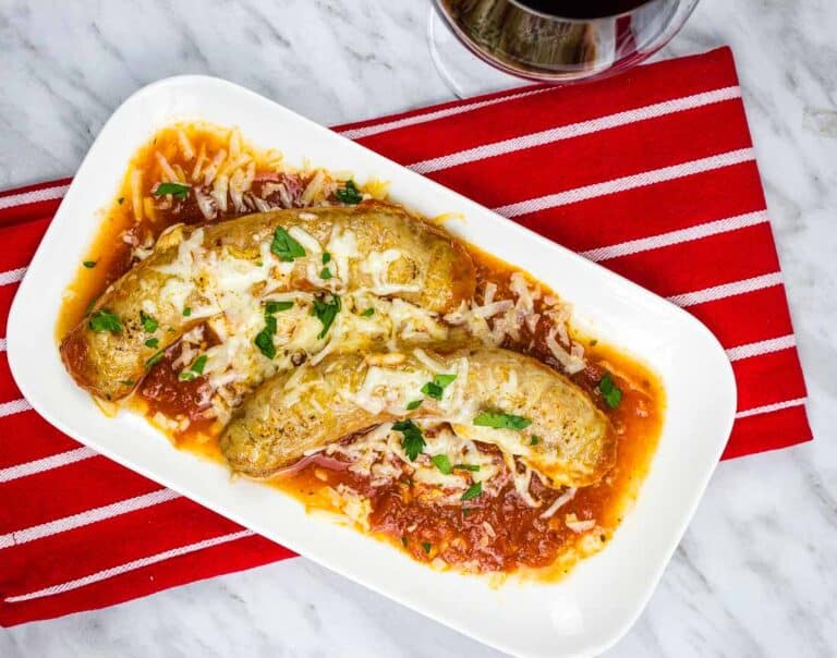 A white plate with Sausage Parmigiana and a glass of wine.