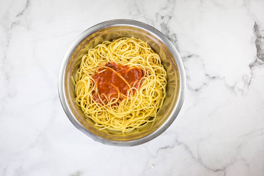 A bowl of spaghetti with sauce on a marble table.