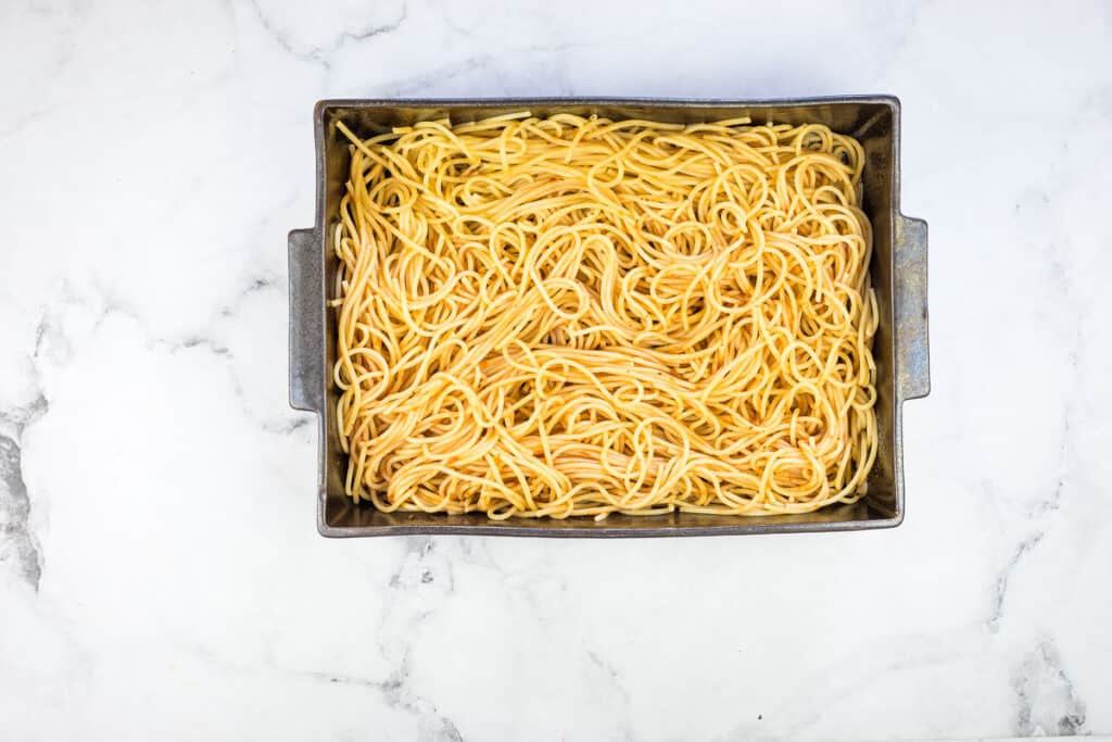 Pasta with sauce in a square pan on a marble countertop.
