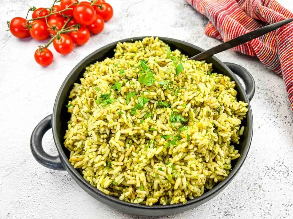 A bowl of green rice with tomatoes and parsley.