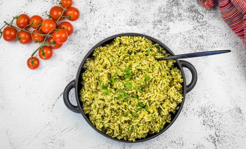 Green rice in a black pan with tomatoes and herbs.