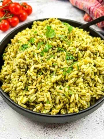Pesto rice in a black bowl with tomatoes.