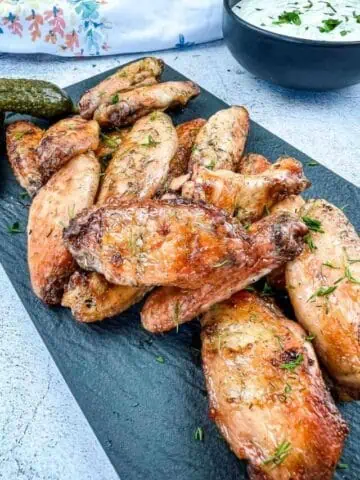 Grilled chicken wings on a plate with pickles and dip.