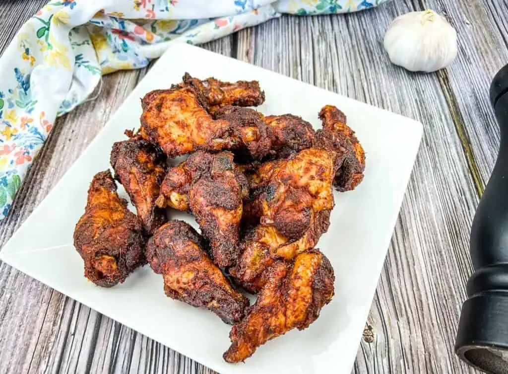 Bbq chicken wings on a white plate with garlic.