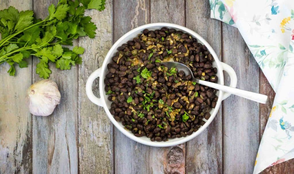 Black beans in a white bowl on a wooden table.