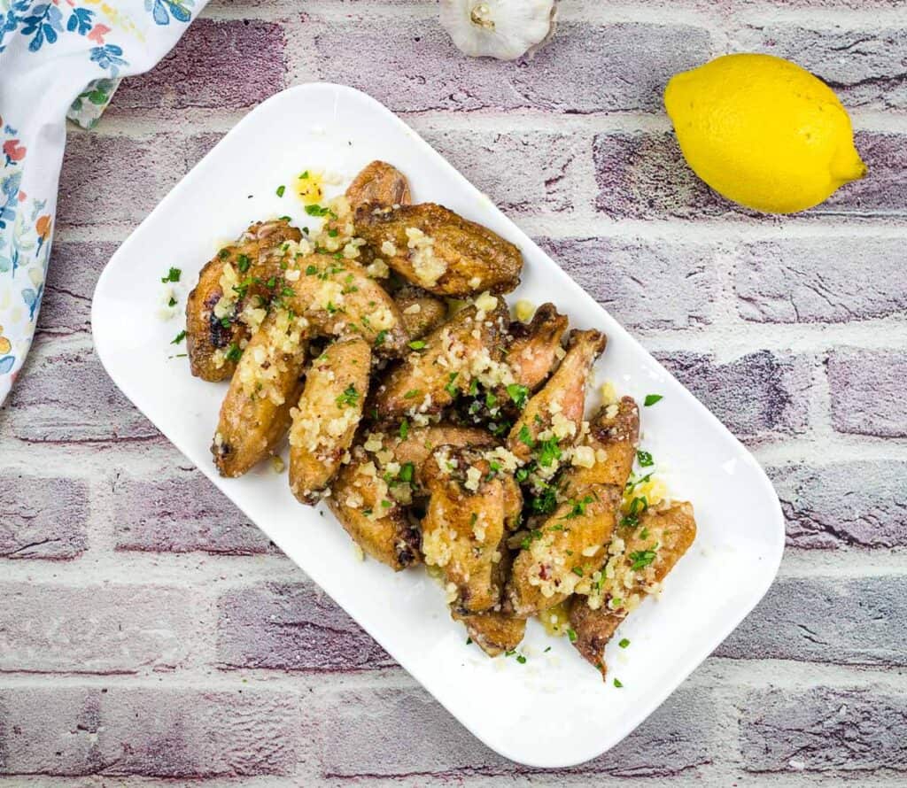 Chicken wings with garlic and lemon on a white plate.