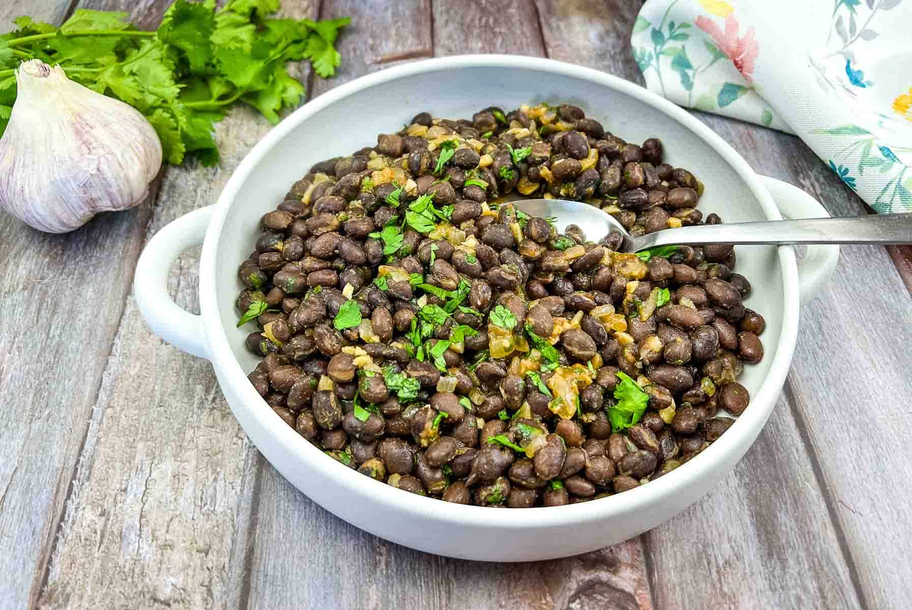 Mexican black beans in a white bowl with parsley and garlic.