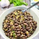 Black beans in a white bowl with garlic and parsley.