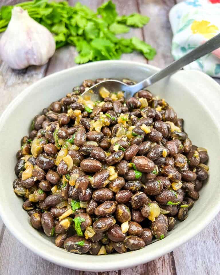 Black beans in a white bowl with garlic and parsley.